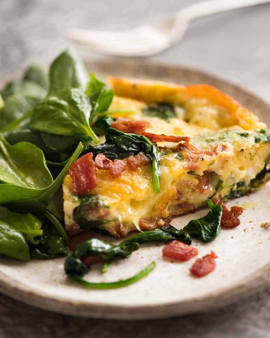 Rodena de frittata con tocino y espinacas en un plato con un lado de la ensalada, listo para comer