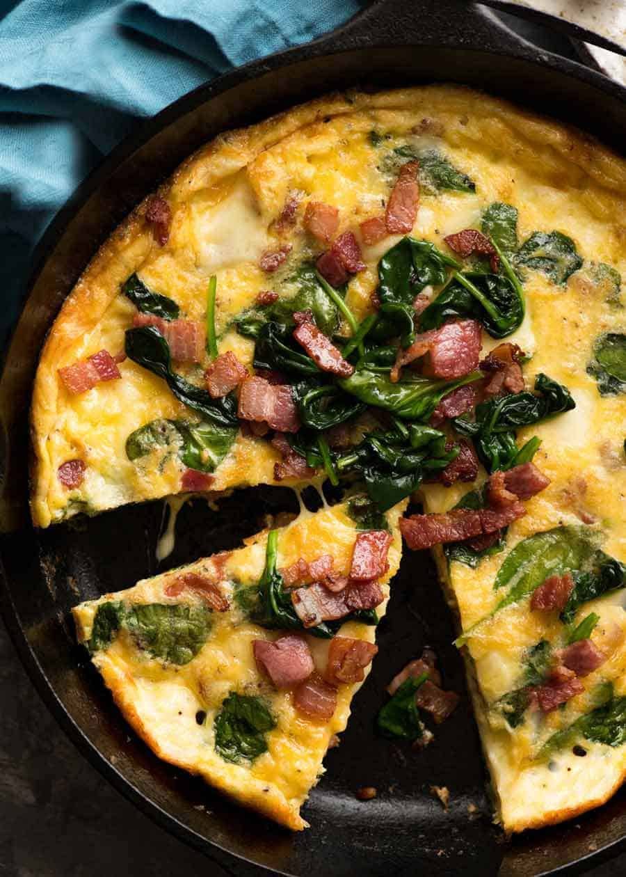 Foto sobre la frittata con tocino y espinacas en una sartén negra, recién salido del horno listo para ser servido