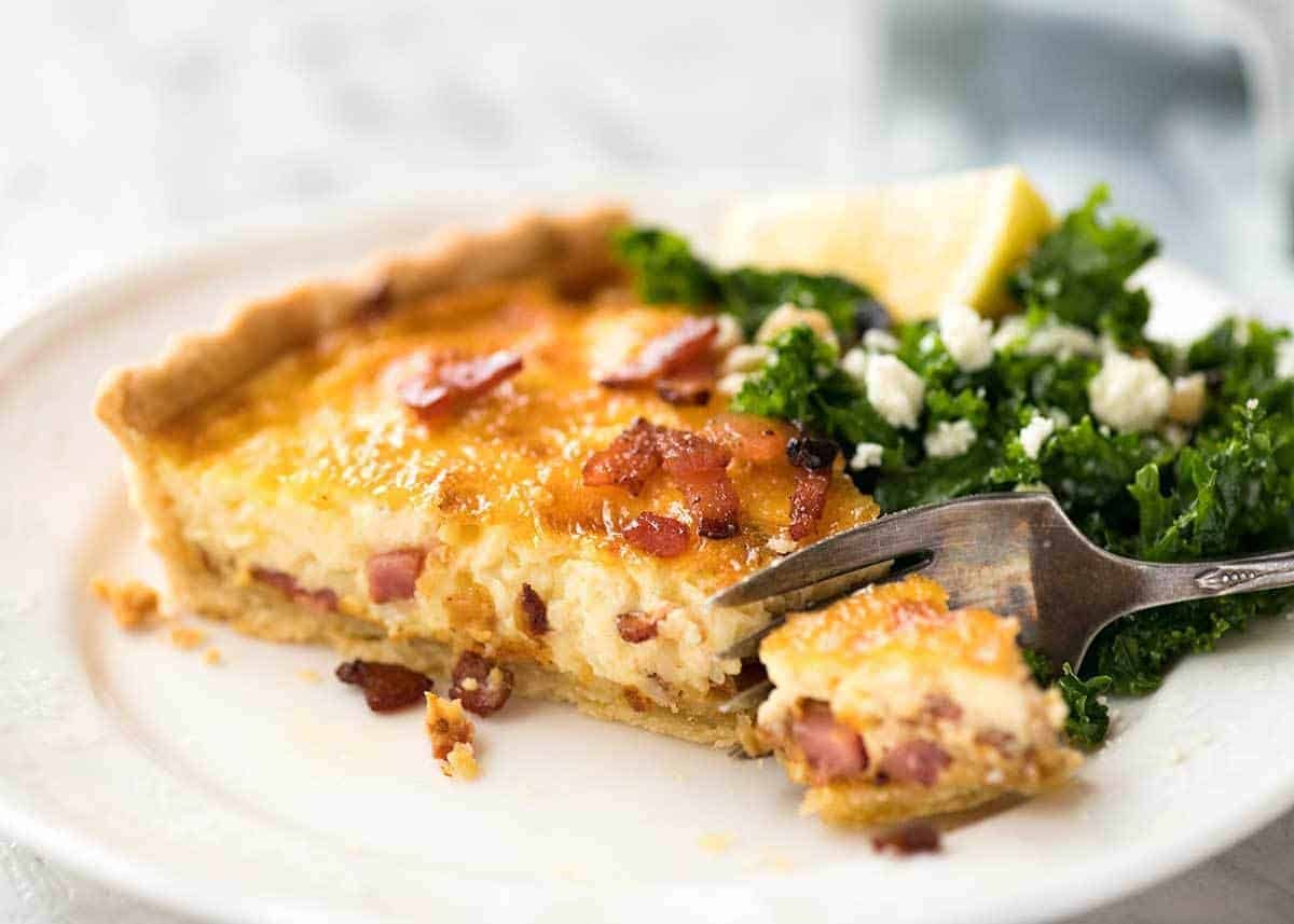 Rebanada de quiche Lorraine en un plato blanco con un tenedor cortándola