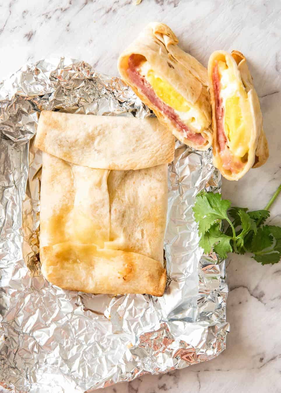 Los bolsillos calientes de jamón, huevo y queso basados ​​en tortillas envueltas en papel de aluminio para cocinar.