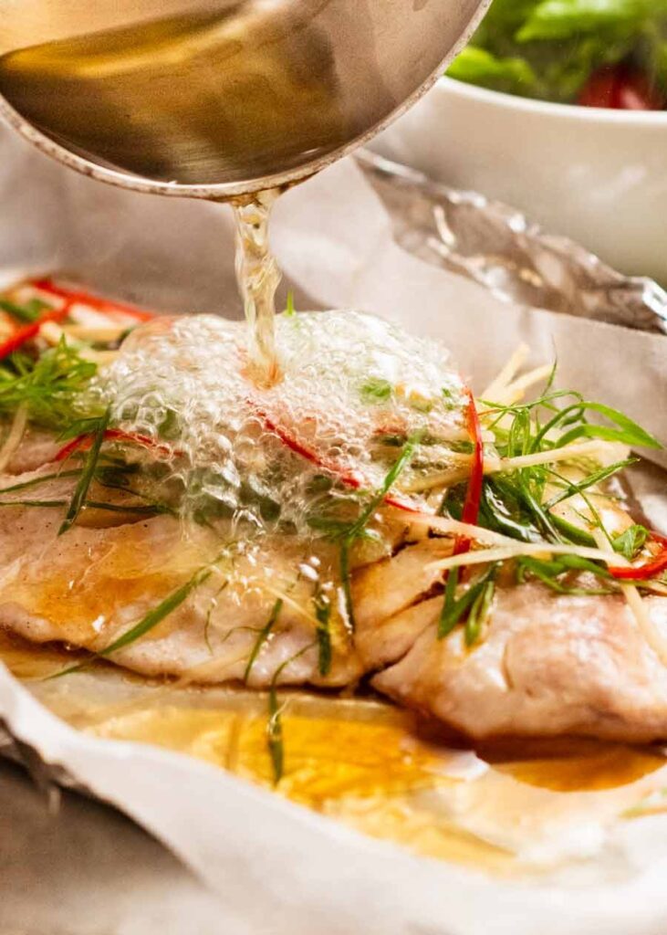 Pouring hot oil over sizzling ginger steamed fish