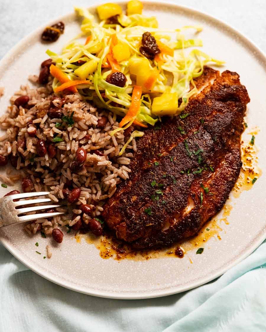Jerk Poisson jamaicano en un plato con una ensalada de chamour y arroz y frijoles jamaicanos