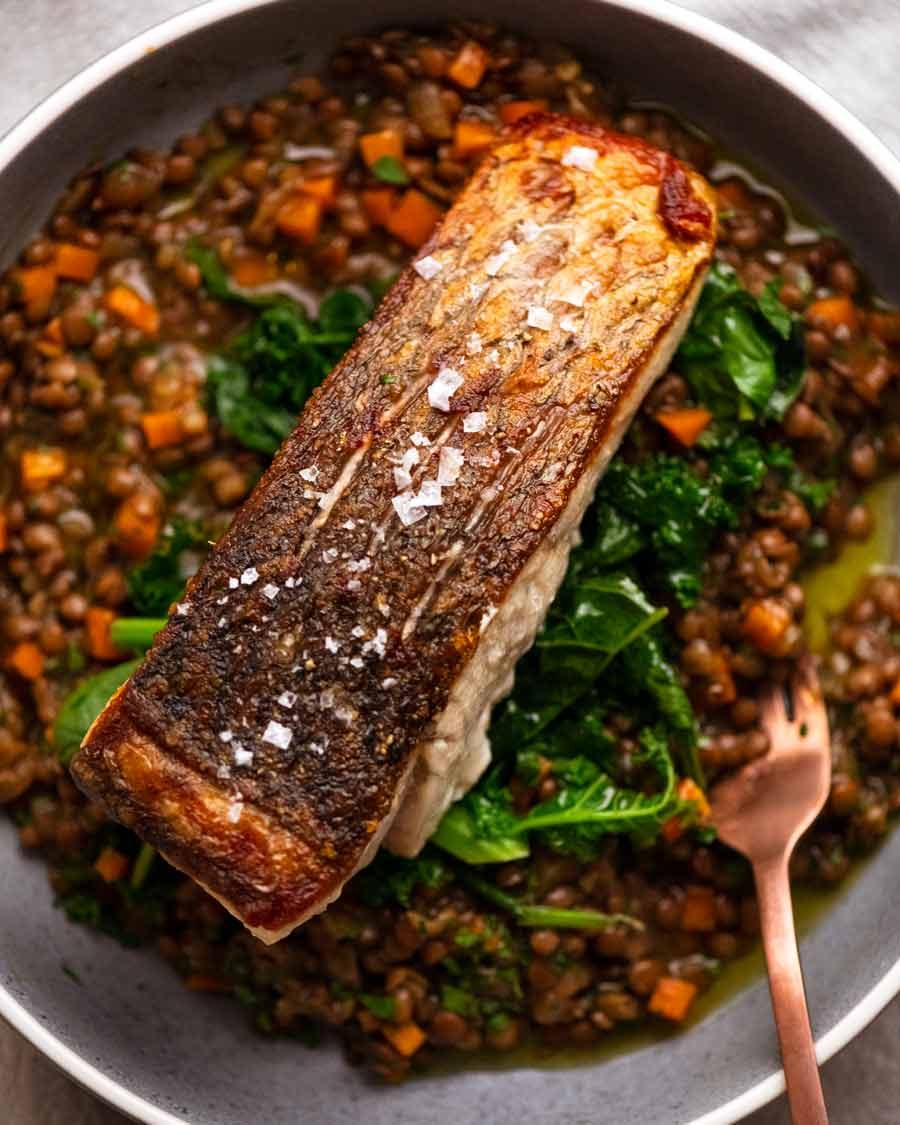 Barramundi de piel crujiente servido con un lado de la lente ragú francesa