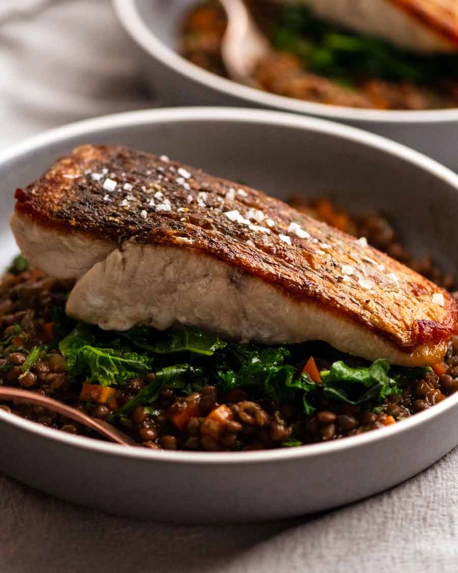 Barramundi de piel crujiente servido con un lado de la lente ragú francesa