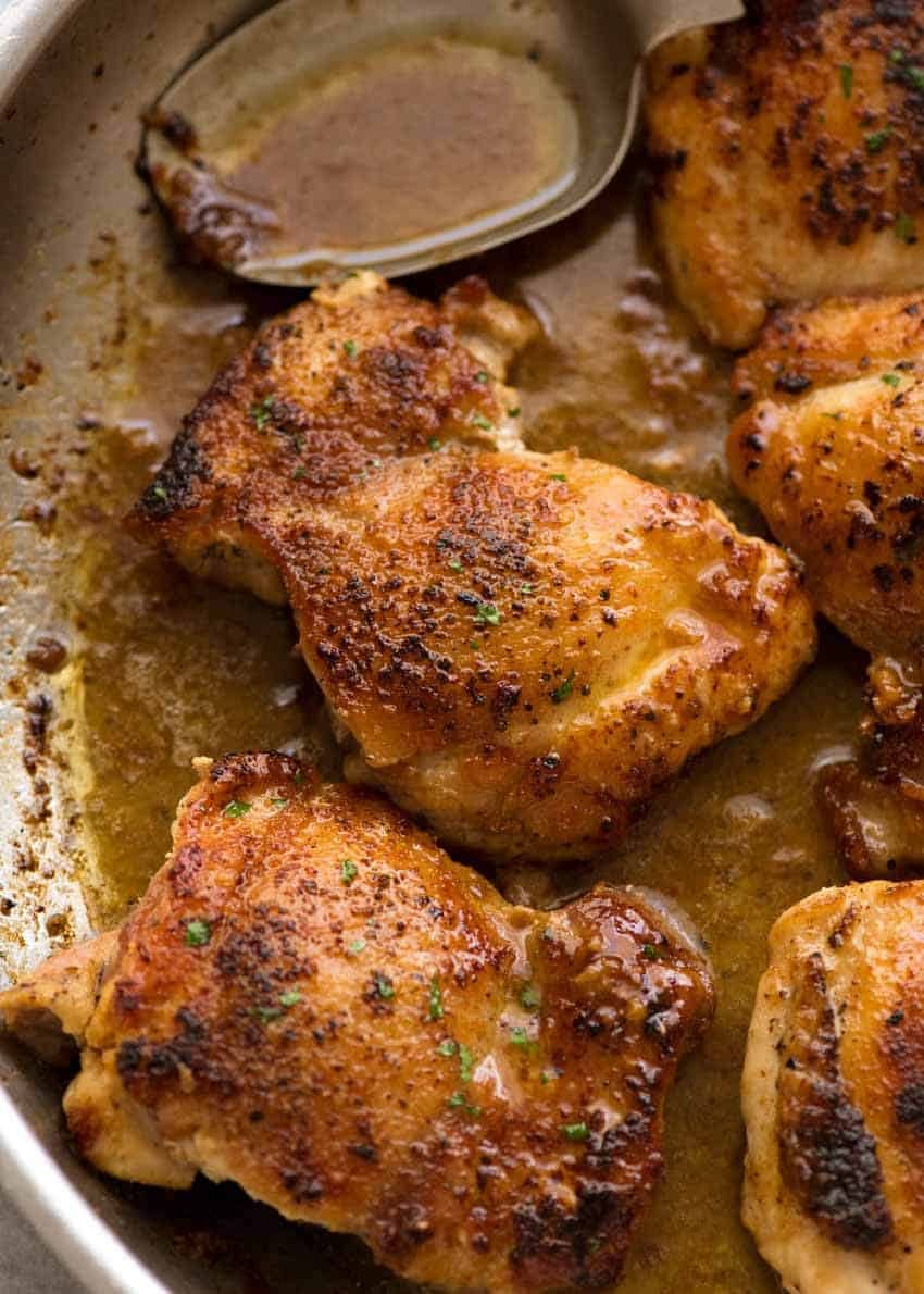Cerrar los muslos de pollo crujientes en una sartén con salsa de mantequilla de ajo, recién salido de la estufa
