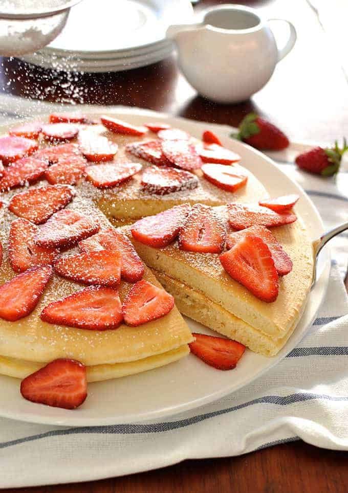 Panqueques gigantes adornados con fresas, rociados con azúcar de glaseado