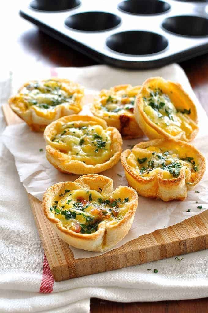Una pila de tazas de tostadas de quiches (tostadas de pan tostadas llenas de adornos de quiche)